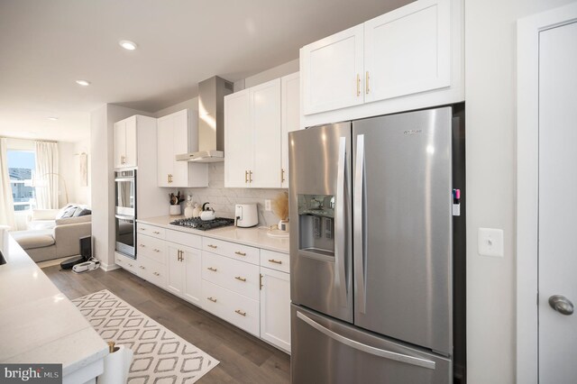 kitchen featuring wall chimney range hood, dark hardwood / wood-style floors, stainless steel appliances, white cabinets, and tasteful backsplash