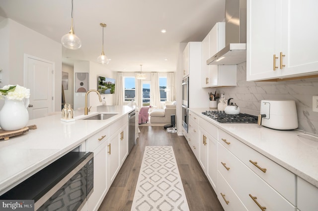 kitchen with wall chimney exhaust hood, sink, decorative light fixtures, appliances with stainless steel finishes, and dark hardwood / wood-style flooring