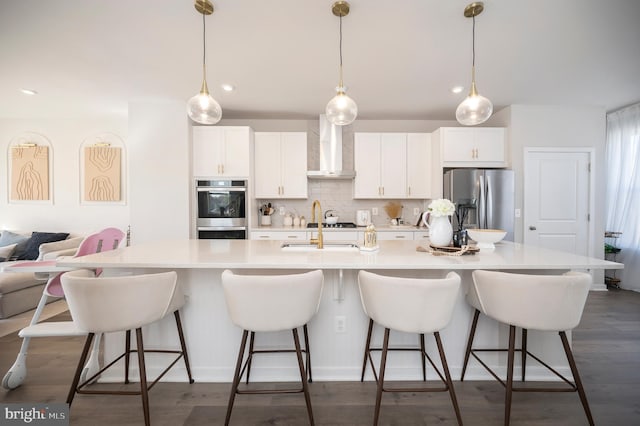 kitchen featuring a large island with sink, tasteful backsplash, wall chimney range hood, a kitchen bar, and stainless steel appliances