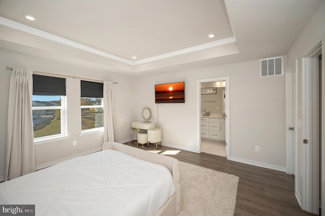 bedroom featuring dark wood-type flooring, ensuite bathroom, and a raised ceiling