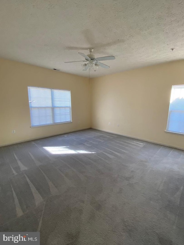 empty room featuring a textured ceiling, ceiling fan, and dark colored carpet