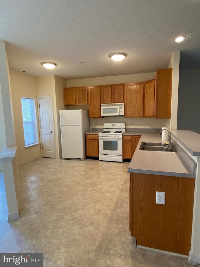 kitchen with a textured ceiling, sink, light tile patterned floors, and white appliances