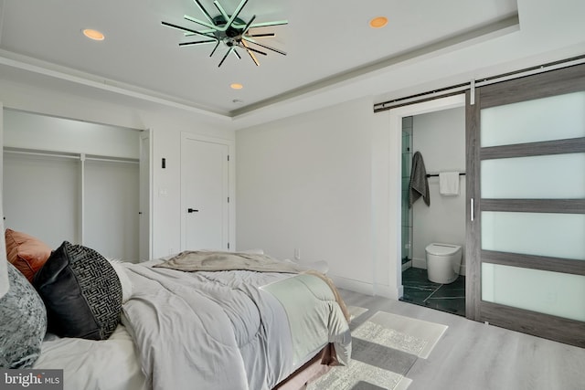 bedroom featuring a closet, a tray ceiling, ensuite bath, hardwood / wood-style floors, and a barn door