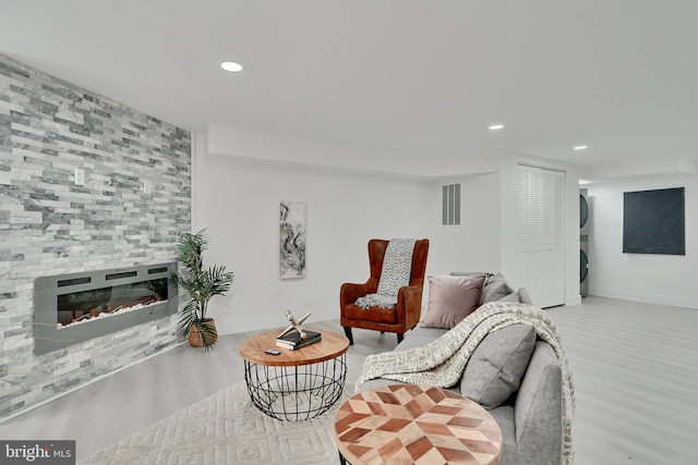 living room featuring stacked washer / dryer, light hardwood / wood-style flooring, and a large fireplace