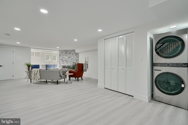 clothes washing area featuring light hardwood / wood-style floors, stacked washer and dryer, and a fireplace