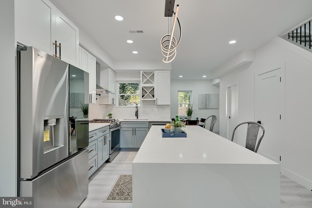 kitchen featuring appliances with stainless steel finishes, sink, backsplash, hanging light fixtures, and light hardwood / wood-style floors