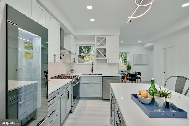 kitchen featuring backsplash, appliances with stainless steel finishes, light hardwood / wood-style floors, wall chimney exhaust hood, and sink