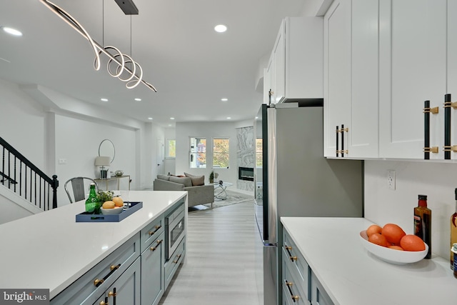 kitchen featuring gray cabinetry, hanging light fixtures, light hardwood / wood-style floors, stainless steel appliances, and white cabinets