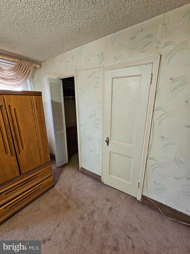 unfurnished bedroom featuring a closet, a textured ceiling, and light colored carpet