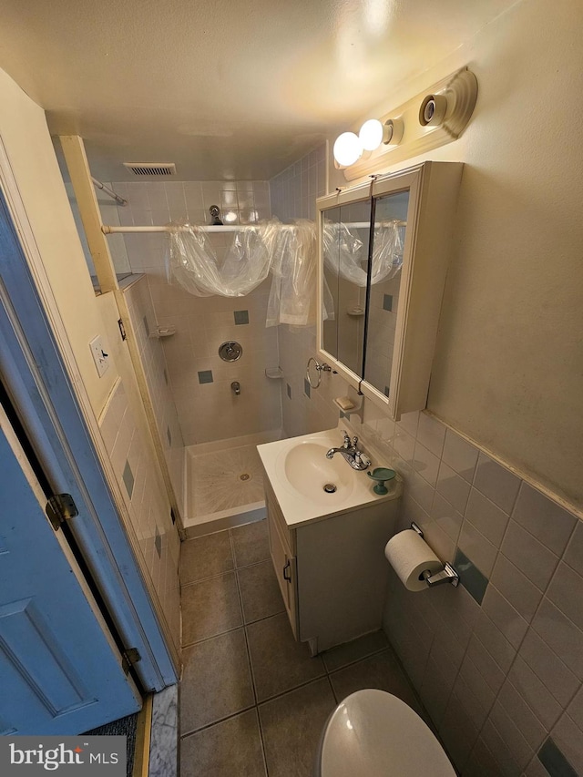 bathroom with a tile shower, toilet, tile patterned floors, tile walls, and vanity