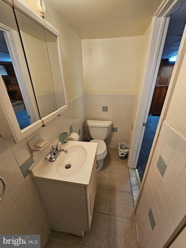 bathroom featuring toilet, vanity, tile patterned floors, and tile walls