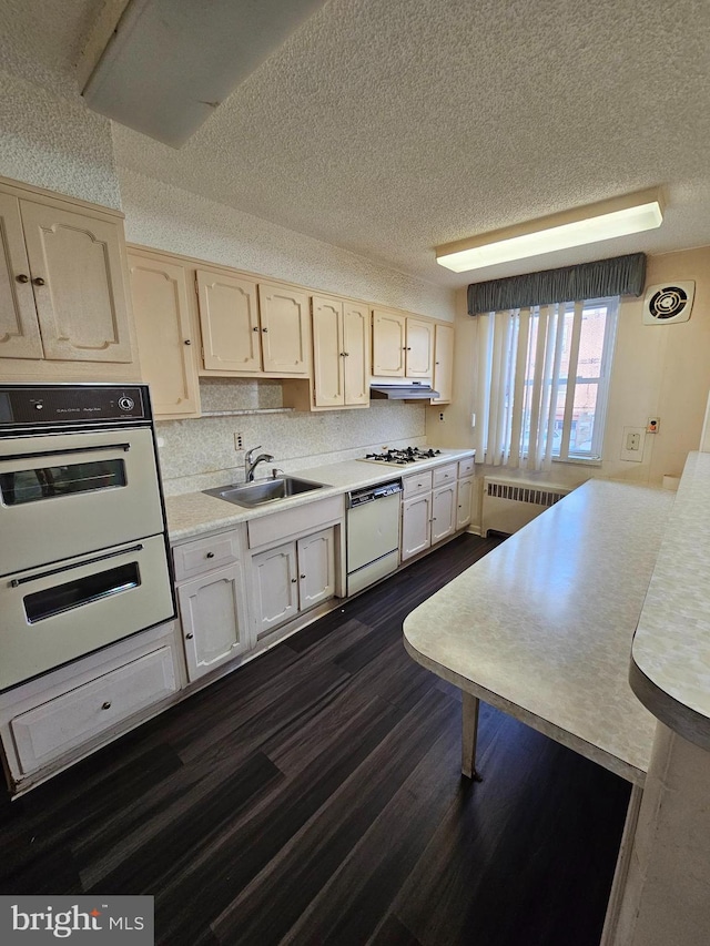 kitchen with white appliances, sink, a textured ceiling, radiator, and dark wood-type flooring