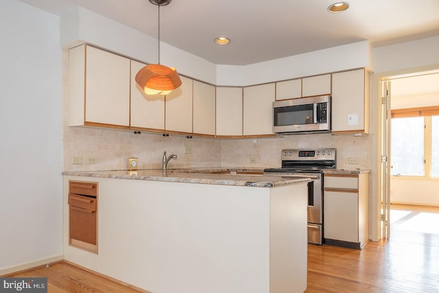 kitchen with tasteful backsplash, kitchen peninsula, pendant lighting, stainless steel appliances, and light hardwood / wood-style floors