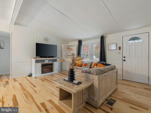 living room with light wood-type flooring, a fireplace, and vaulted ceiling with beams