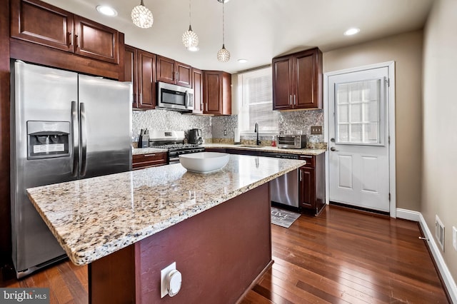 kitchen with stainless steel appliances, a center island, decorative light fixtures, light stone counters, and dark hardwood / wood-style flooring