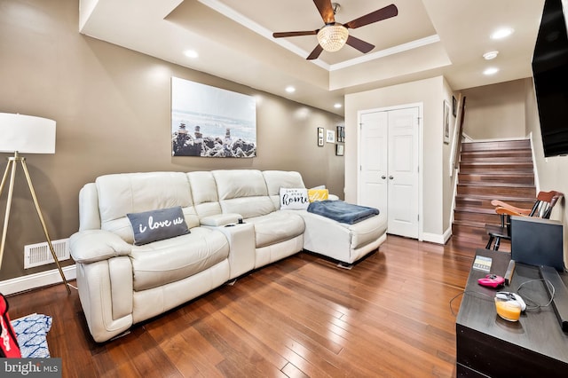 living room featuring ornamental molding, ceiling fan, wood-type flooring, and a raised ceiling