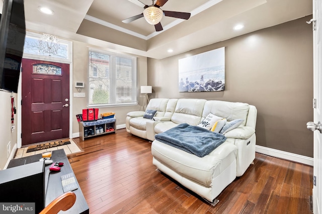 living room with ornamental molding, dark wood-type flooring, ceiling fan, and a raised ceiling