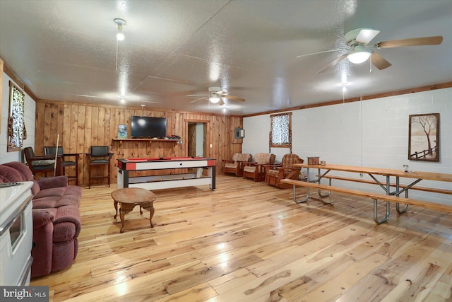 rec room featuring light hardwood / wood-style flooring, ceiling fan, a textured ceiling, and wood walls