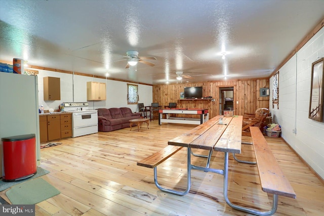 dining room with wooden walls, a textured ceiling, light wood-type flooring, and ceiling fan