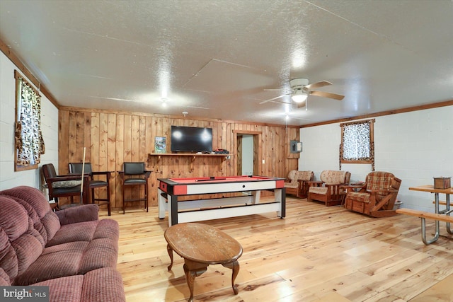 living room with light hardwood / wood-style flooring, ceiling fan, a textured ceiling, and wood walls