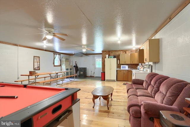 playroom with pool table, a wood stove, a textured ceiling, ceiling fan, and light hardwood / wood-style flooring