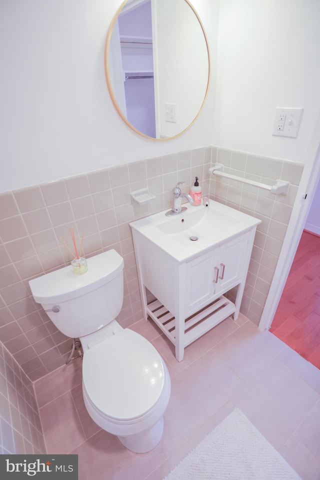 half bath with tile walls, tile patterned floors, toilet, wainscoting, and vanity