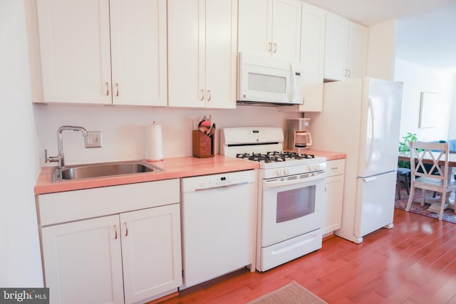 kitchen featuring white appliances, a sink, light wood-style flooring, light countertops, and white cabinetry