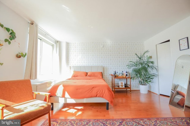 bedroom featuring wallpapered walls, wood finished floors, and an accent wall