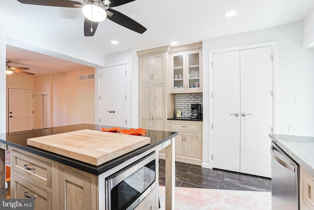 kitchen with decorative backsplash, appliances with stainless steel finishes, a kitchen island, and light brown cabinetry