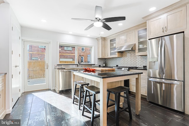 kitchen featuring a kitchen island, a breakfast bar, tasteful backsplash, ceiling fan, and stainless steel appliances