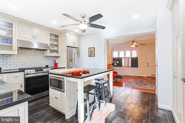 kitchen with decorative backsplash, appliances with stainless steel finishes, ceiling fan, dark hardwood / wood-style floors, and a breakfast bar area