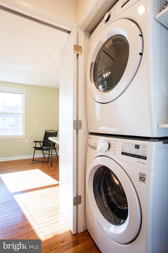 clothes washing area with wood-type flooring and stacked washer and dryer