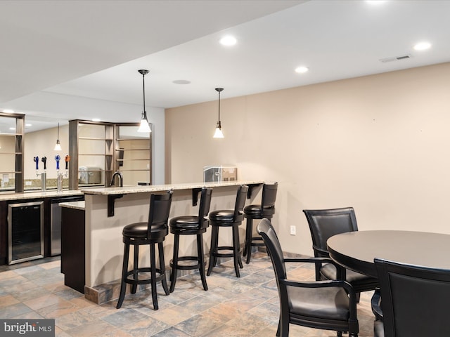 bar with dishwasher, light stone countertops, pendant lighting, and beverage cooler