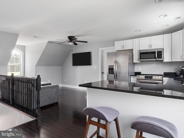 kitchen with a breakfast bar area, kitchen peninsula, white cabinetry, appliances with stainless steel finishes, and dark hardwood / wood-style flooring