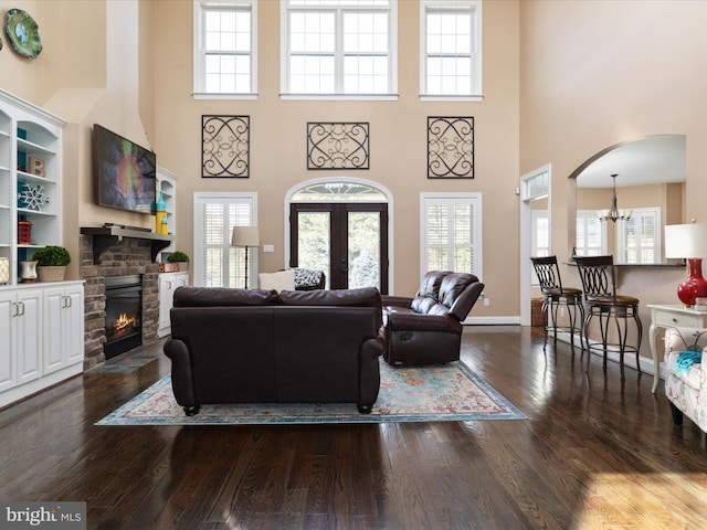 living room with a high ceiling, a notable chandelier, a fireplace, and dark hardwood / wood-style flooring