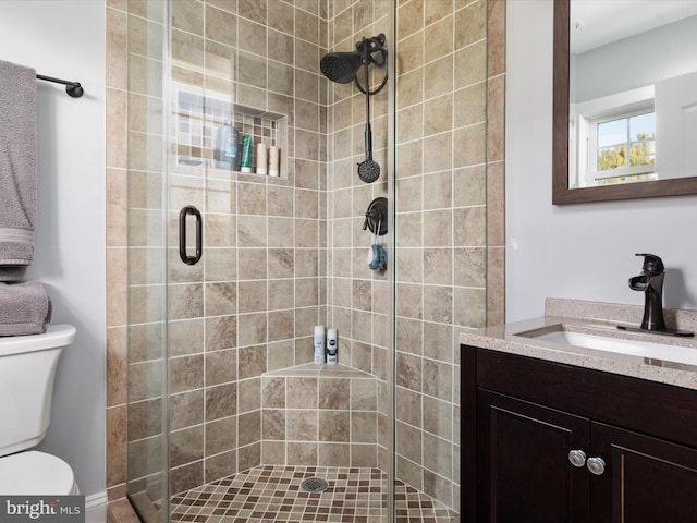 bathroom featuring a shower with door, vanity, and toilet