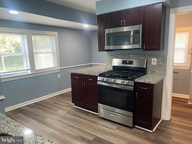 kitchen with backsplash, light wood-type flooring, light stone counters, dark brown cabinetry, and stainless steel appliances