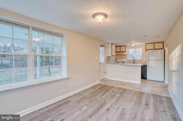 kitchen with kitchen peninsula, white appliances, light hardwood / wood-style flooring, and a healthy amount of sunlight