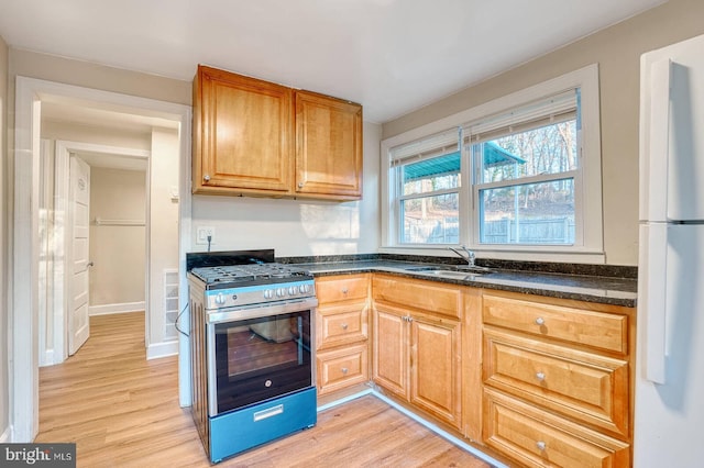 kitchen featuring stainless steel range with gas cooktop, sink, light hardwood / wood-style floors, and white refrigerator