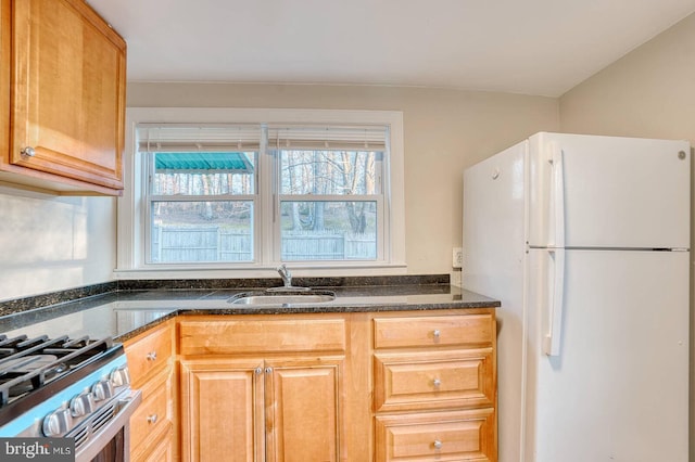 kitchen with dark stone countertops, sink, white fridge, and stainless steel stove