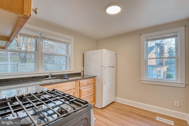 kitchen featuring light brown cabinets, stove, sink, light wood-type flooring, and white fridge