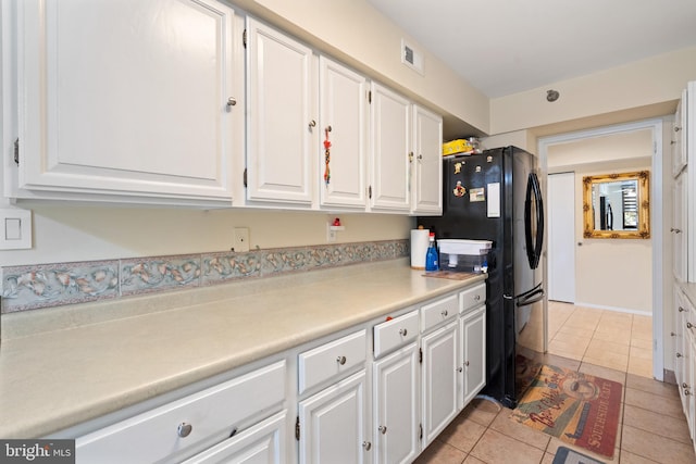 kitchen with white cabinets, black refrigerator, and light tile patterned floors