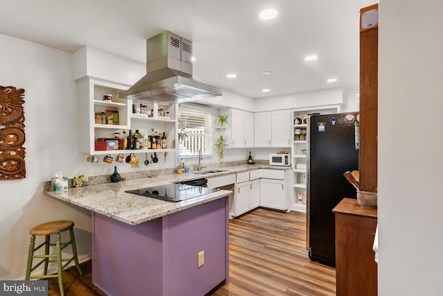 kitchen featuring kitchen peninsula, island exhaust hood, a kitchen bar, light wood-type flooring, and black appliances