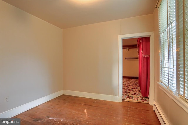 empty room with a baseboard heating unit, baseboards, and wood finished floors