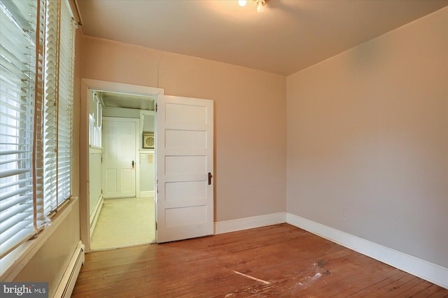 empty room with hardwood / wood-style flooring, baseboards, and a baseboard heating unit