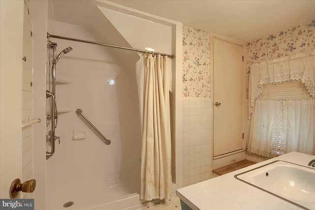 bathroom with a stall shower, wainscoting, a sink, and wallpapered walls