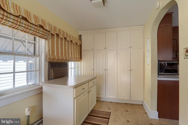 kitchen with arched walkways, white cabinets, light countertops, and a center island