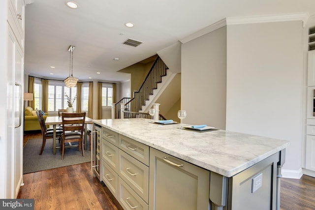 kitchen with wine cooler, hanging light fixtures, light stone counters, dark wood-type flooring, and a center island