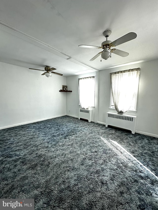 empty room featuring dark colored carpet, ceiling fan, and radiator