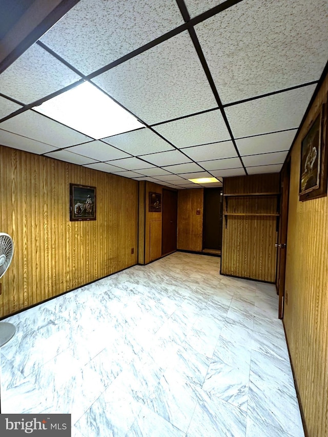 basement featuring a drop ceiling and wood walls